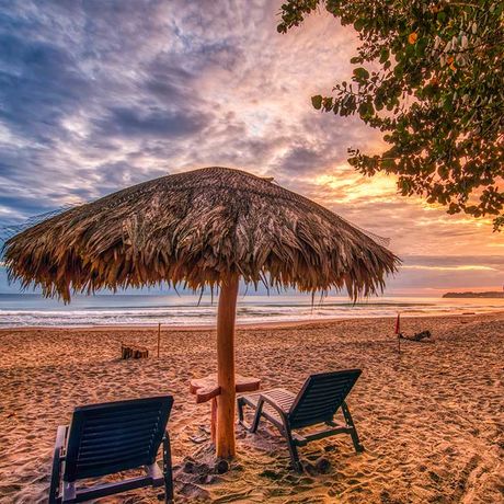 Blick auf zwei Liegen unter einem Sonnenschirm am Strand der Strandunterkunft Banana Azul
